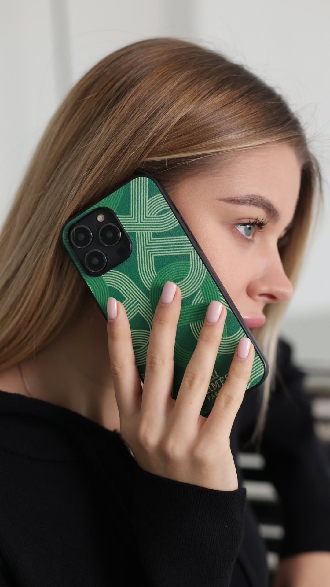 Woman holding a phone with a green case against a neutral background